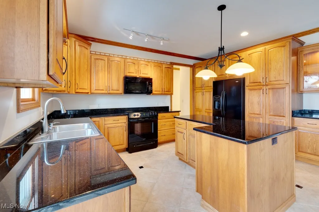 Kitchen with decorative light fixtures, sink, dark stone counters, a center island, and black appliances