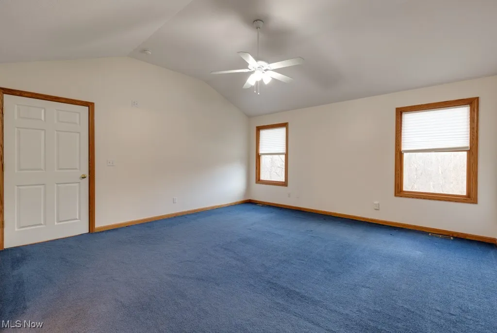 Carpeted spare room featuring ceiling fan and vaulted ceiling