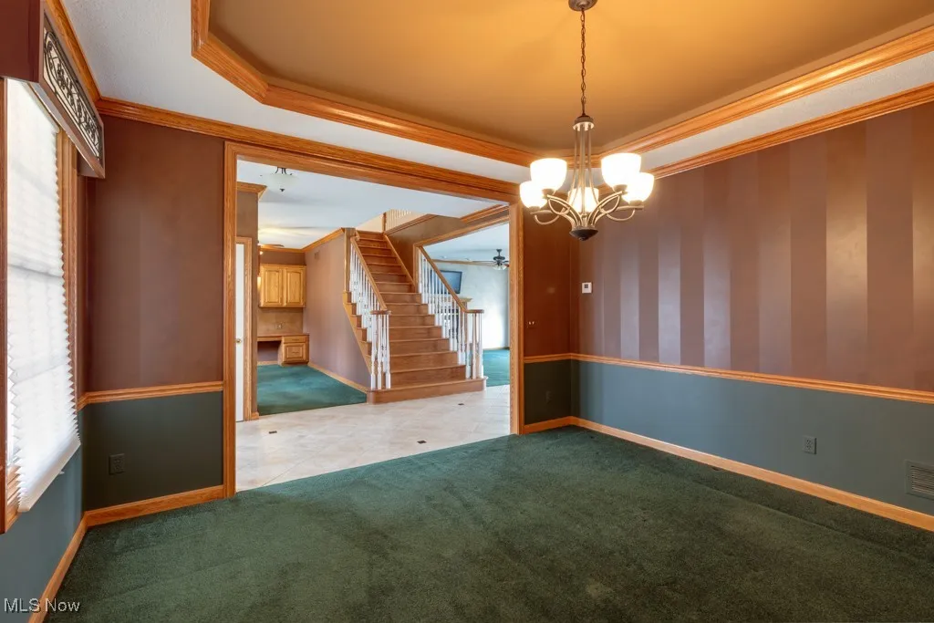 Spare room with crown molding, a tray ceiling, carpet floors, and an inviting chandelier