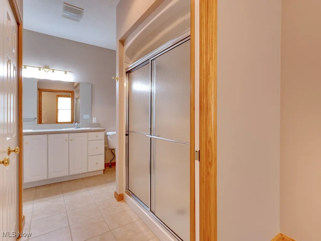 Bathroom featuring tile patterned flooring, vanity, toilet, and a shower with shower door