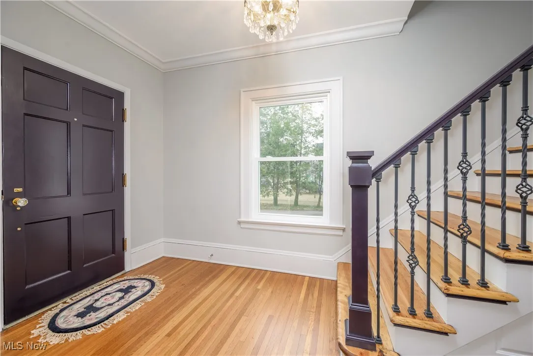 Foyer featuring wood-flooring, ornamental molding, and a notable chandelier