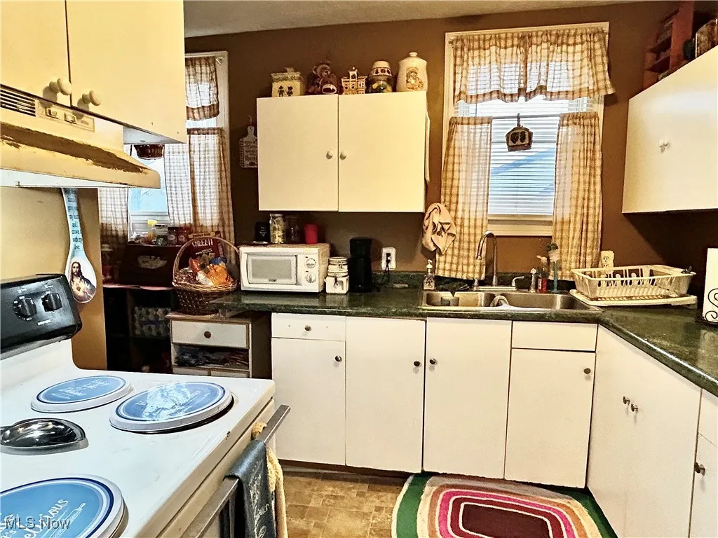 Kitchen featuring range with electric cooktop, white cabinetry, and sink