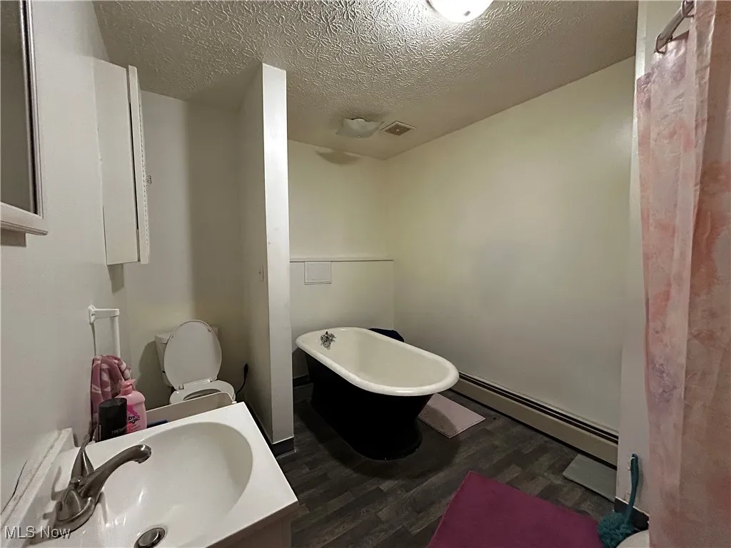 Bathroom featuring hardwood / wood-style flooring, a textured ceiling, a baseboard radiator, a tub, and toilet