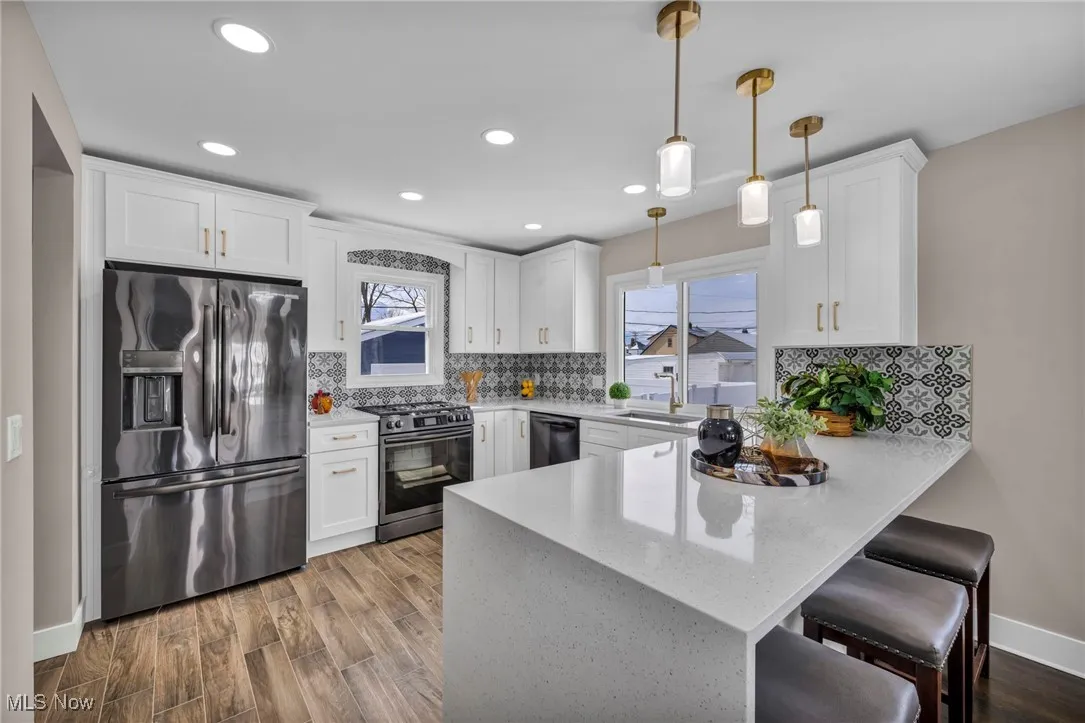 Kitchen with wood finished floors, appliances with stainless steel finishes, a peninsula, and white cabinets