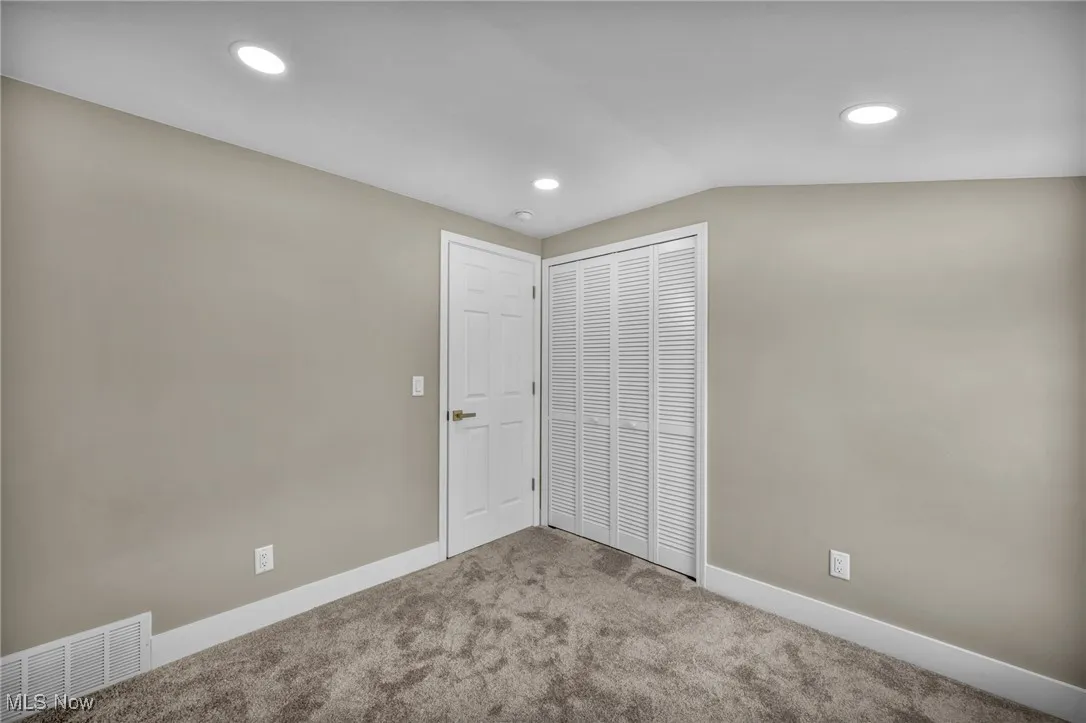 Unfurnished bedroom featuring lofted ceiling, light colored carpet, and a closet