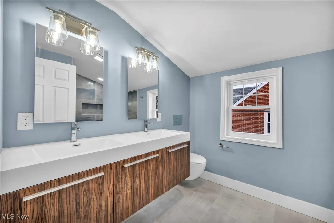 Bathroom featuring vanity, vaulted ceiling, tile patterned floors, and toilet