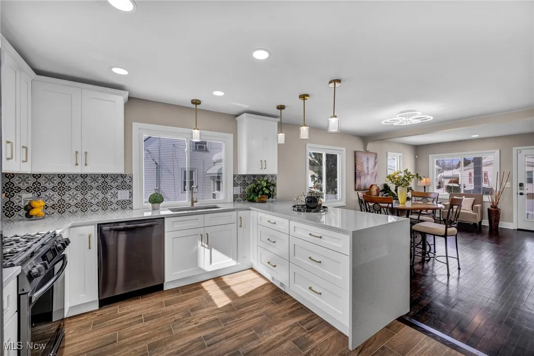 Kitchen with range with gas stovetop, a peninsula, stainless steel dishwasher, dark wood-style floors, and a sink