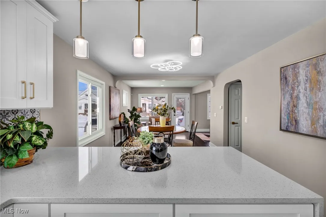 Kitchen featuring light stone counters, arched walkways, white cabinets, and hanging light fixtures
