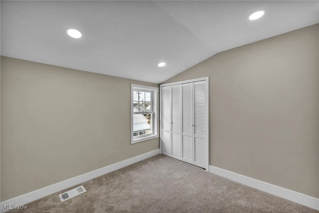 Unfurnished bedroom with vaulted ceiling, a closet, and carpet