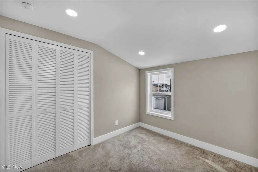 Unfurnished bedroom featuring light colored carpet, lofted ceiling, and a closet