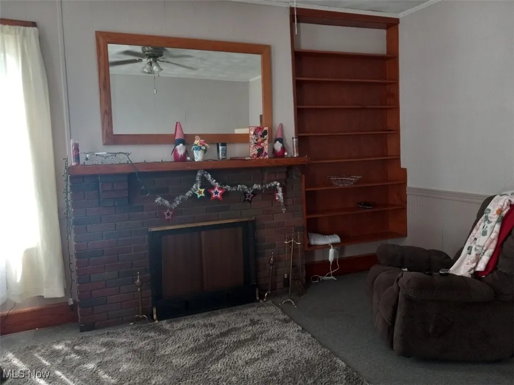 Living room featuring carpet flooring, crown molding, a fireplace, and ceiling fan