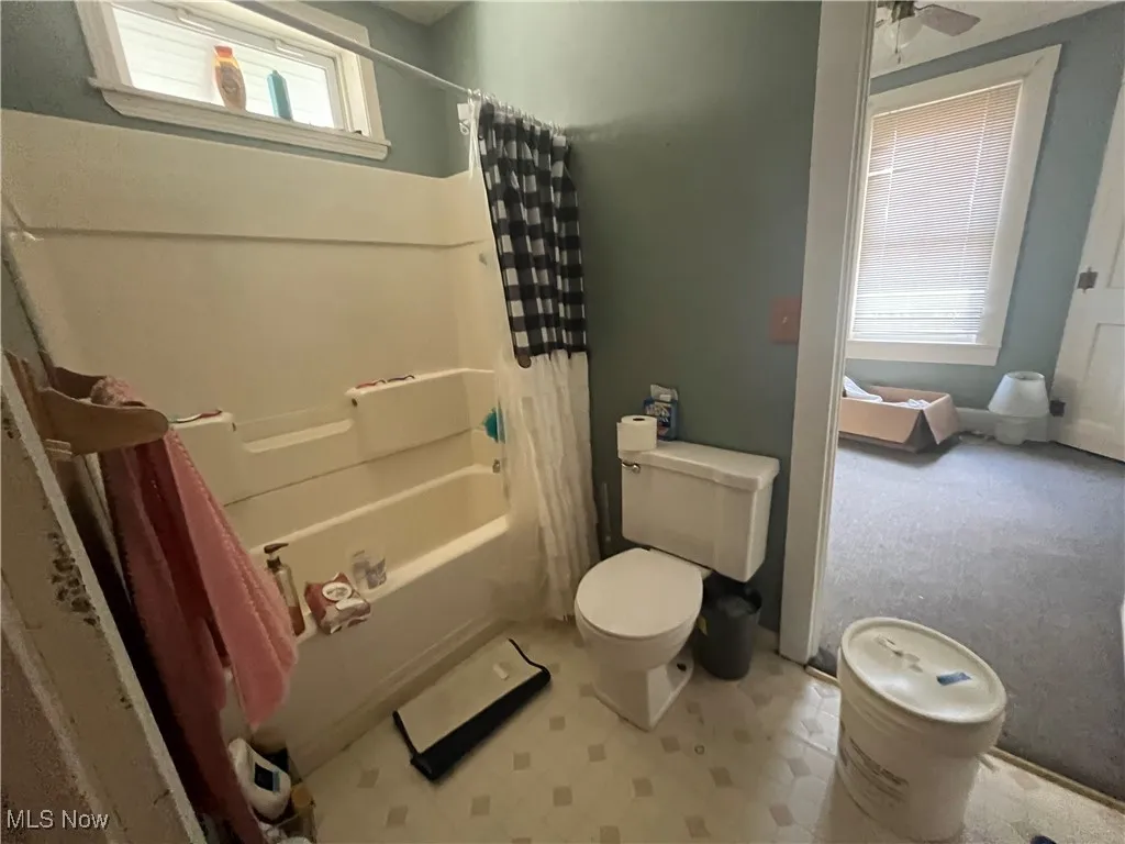 Bathroom featuring toilet, shower / bath combo, and ceiling fan
