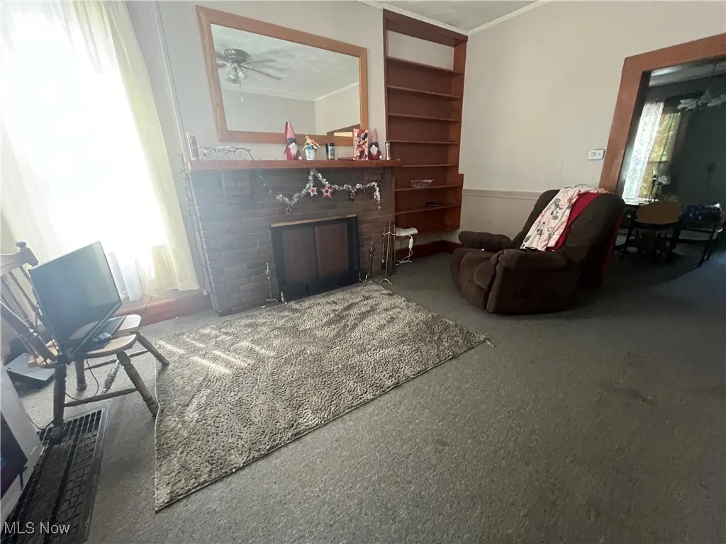 Living room featuring carpet floors, ceiling fan, crown molding, and a brick fireplace