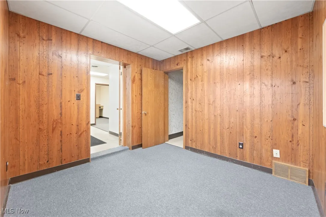Unfurnished room with dark carpet, wooden walls, and a drop ceiling