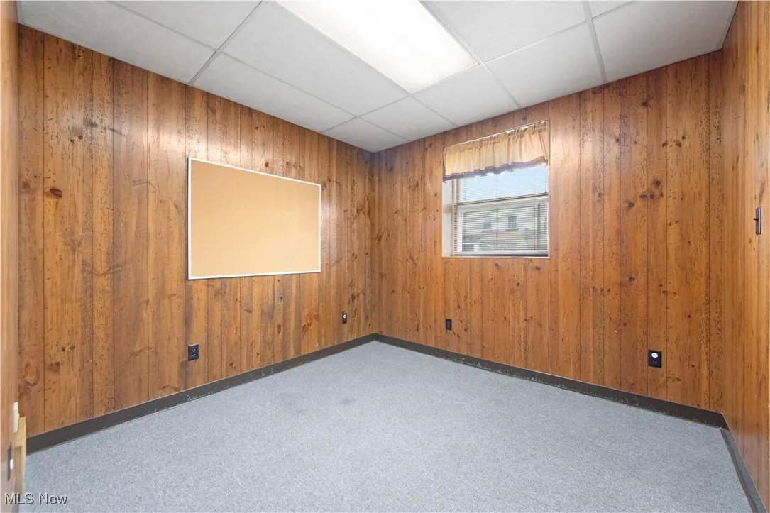 Empty room with a paneled ceiling, carpet flooring, and wood walls