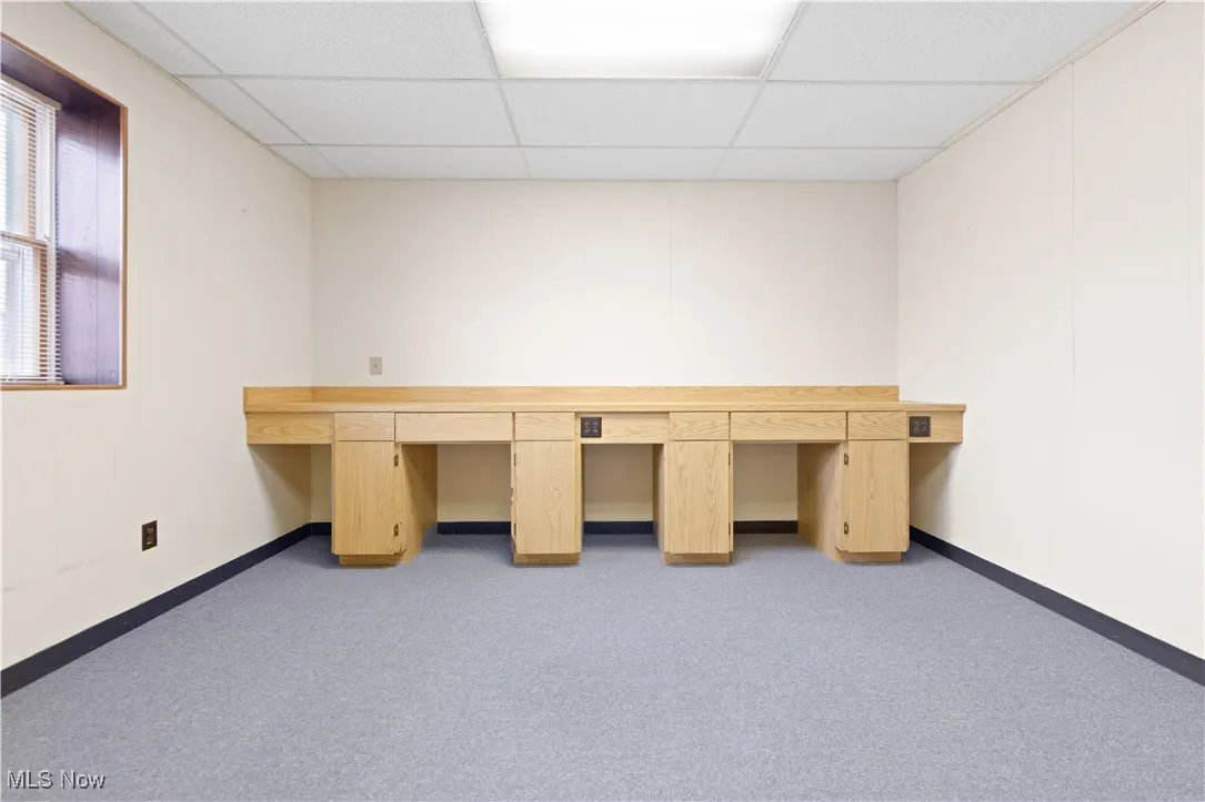 Unfurnished office with a paneled ceiling, light carpet, and built in desk