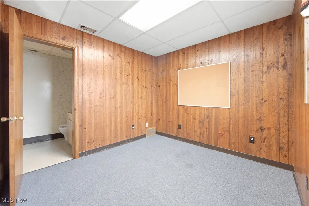 Empty room with a paneled ceiling, wooden walls, and carpet flooring
