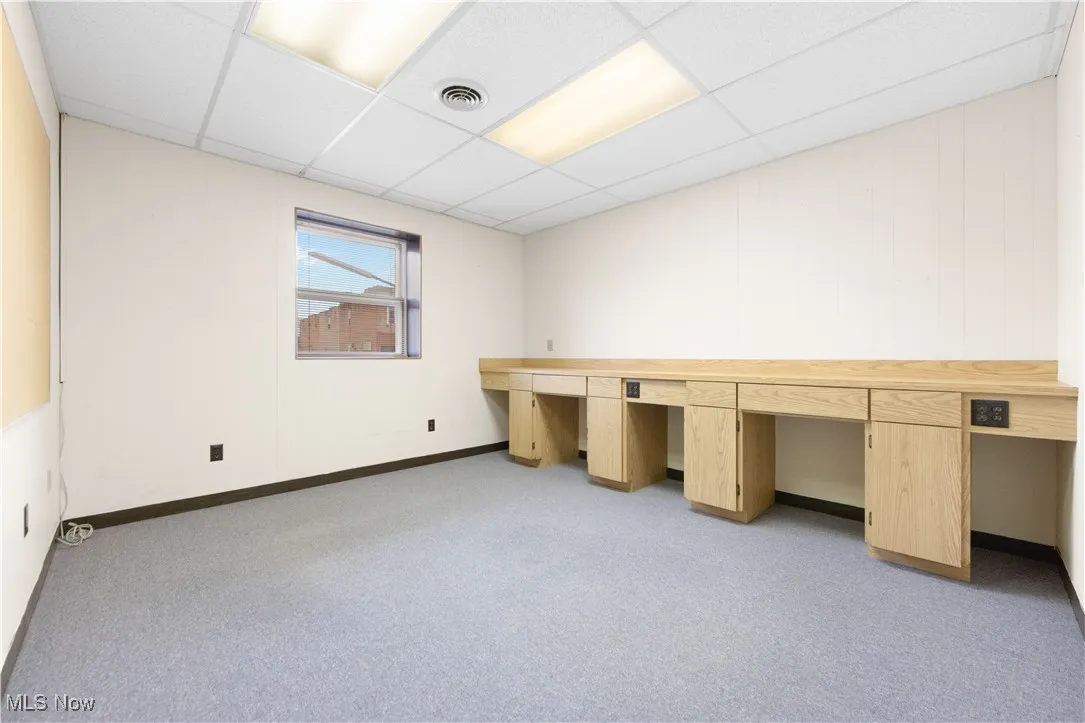 Unfurnished office with light carpet, built in desk, and a paneled ceiling