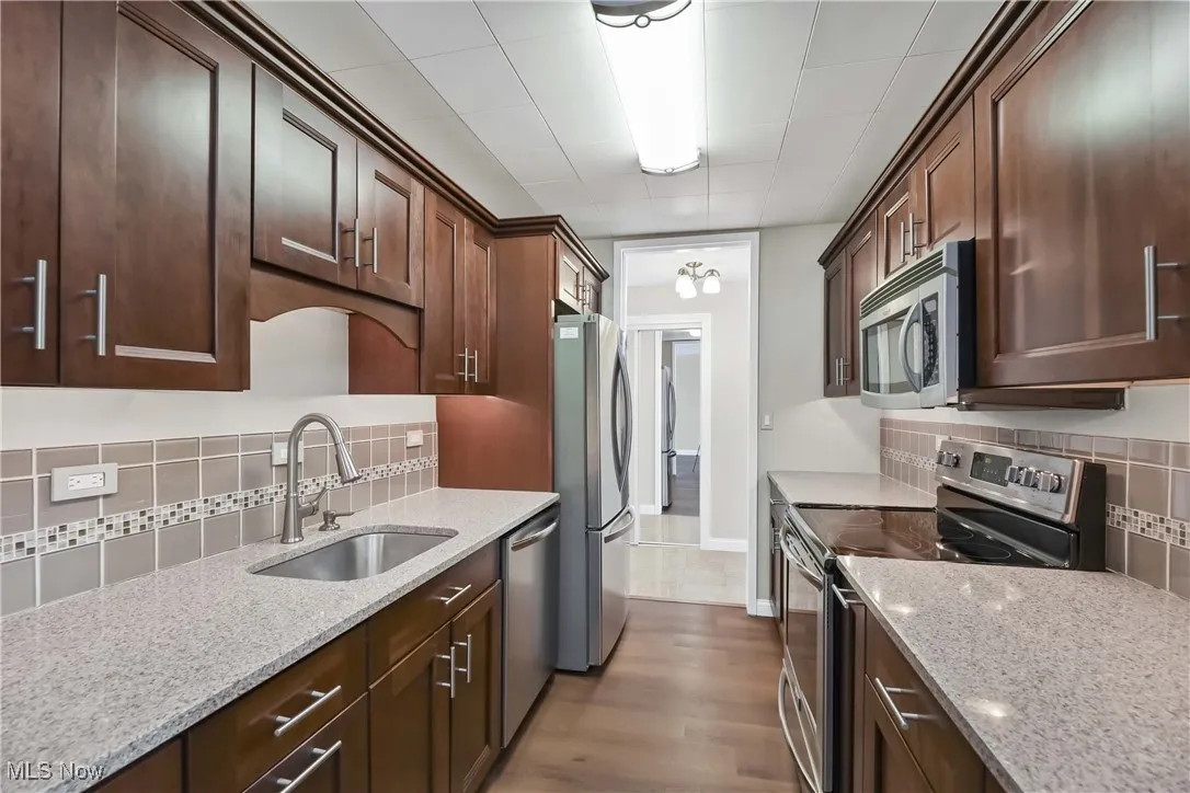 Kitchen with light stone counters, sink, stainless steel appliances, and dark brown cabinetry