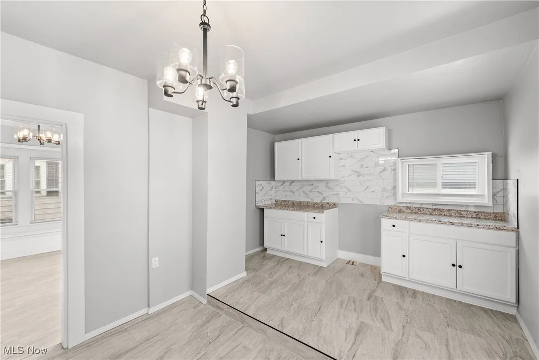 Kitchen with white cabinetry, backsplash, an inviting chandelier, and decorative light fixtures