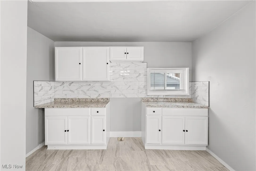 Kitchen with white cabinetry, light stone countertops, and decorative backsplash