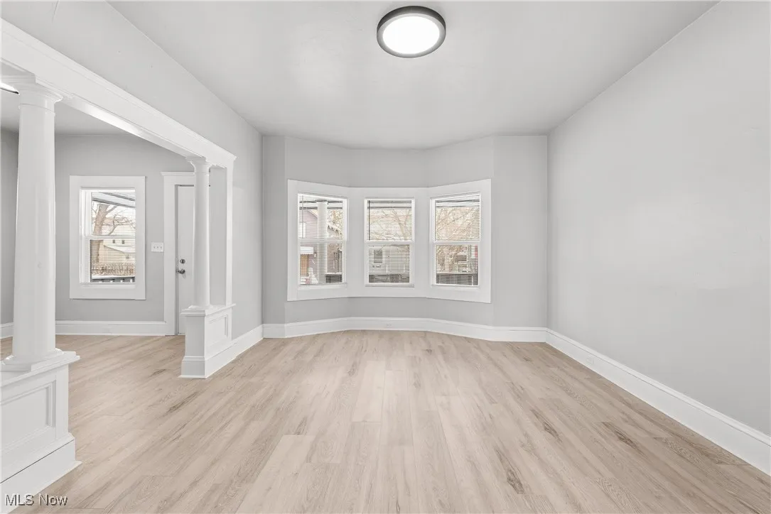 Empty room with light hardwood / wood-style flooring, ornate columns, and a healthy amount of sunlight