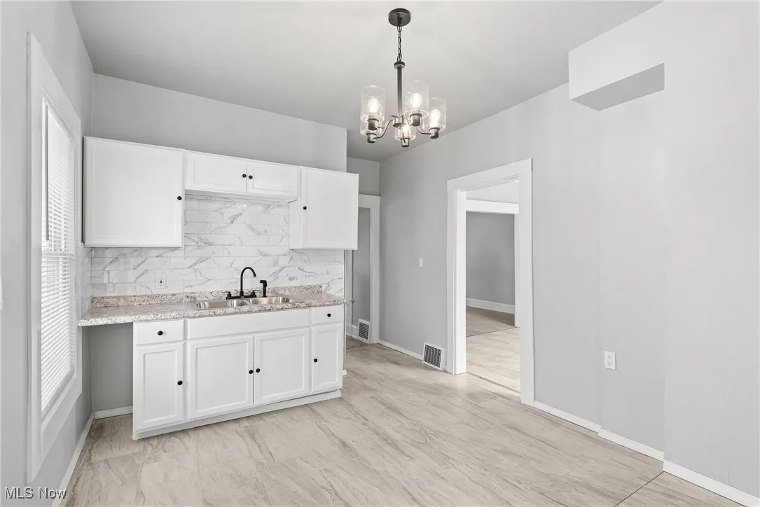 Kitchen featuring light stone countertops, decorative light fixtures, backsplash, sink, and white cabinetry