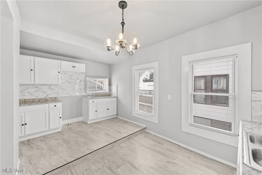 Kitchen featuring white cabinetry, hanging light fixtures, a notable chandelier, sink, and tasteful backsplash