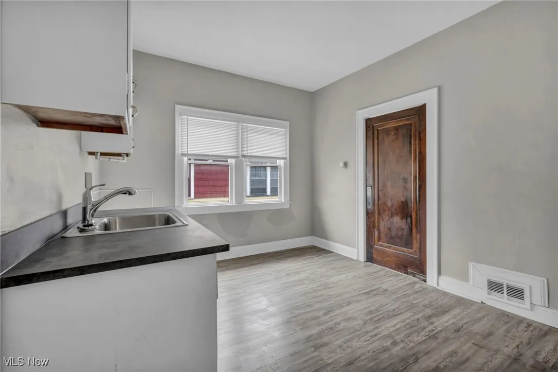 Kitchen featuring dark countertops, wood finished floors, visible vents, a sink, and baseboards
