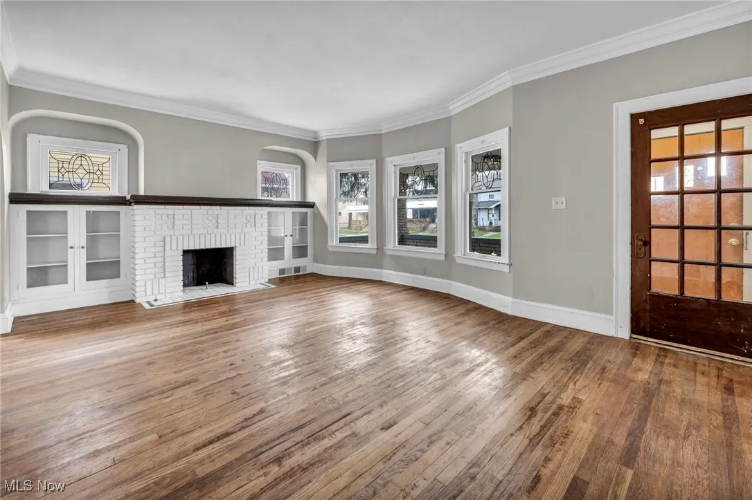 Unfurnished living room featuring a brick fireplace, wood finished floors, a healthy amount of sunlight, and ornamental molding
