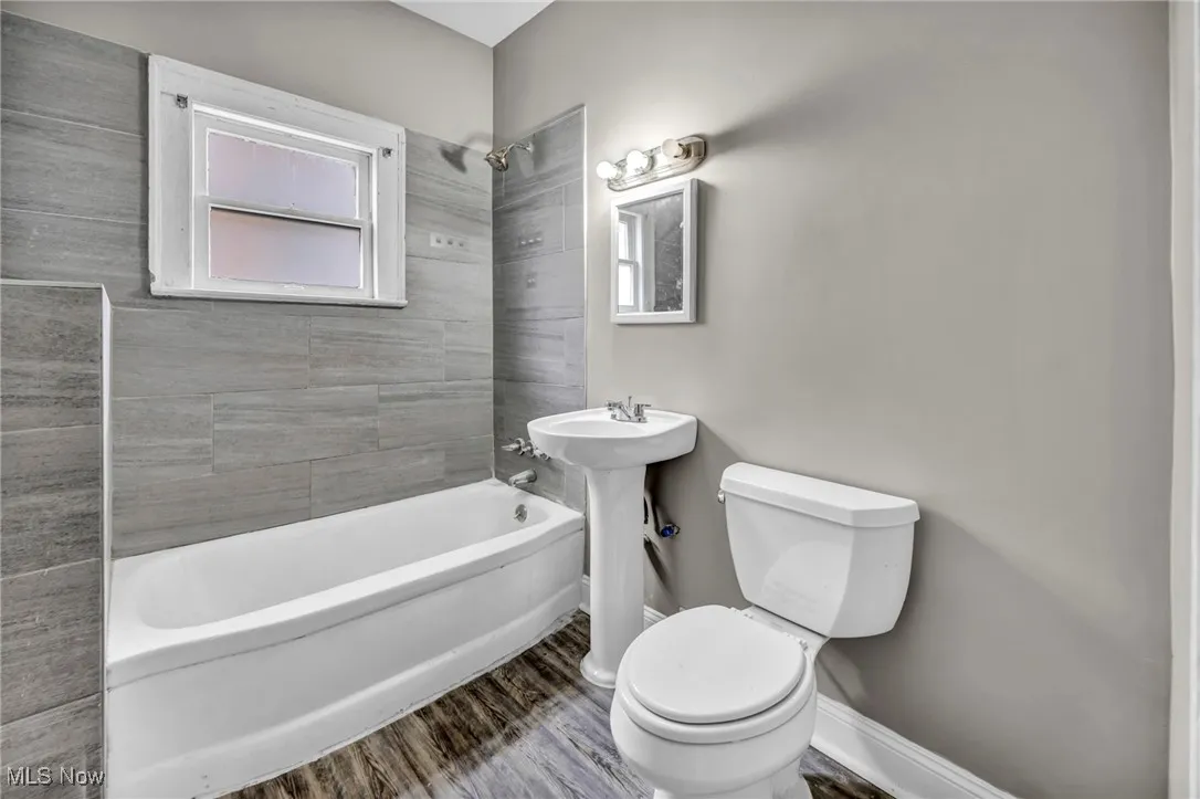 Bathroom with a sink, bathtub / shower combination, a healthy amount of sunlight, baseboards, and toilet