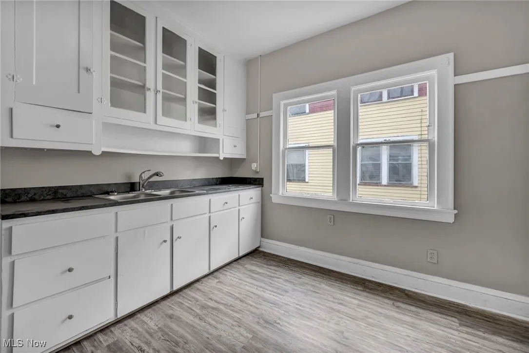 Kitchen featuring dark countertops, a sink, light wood-type flooring, baseboards, and white cabinetry