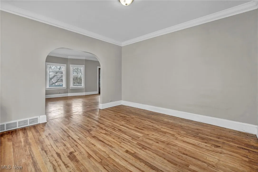 Spare room featuring hardwood / wood-style floors, visible vents, ornamental molding, arched walkways, and baseboards