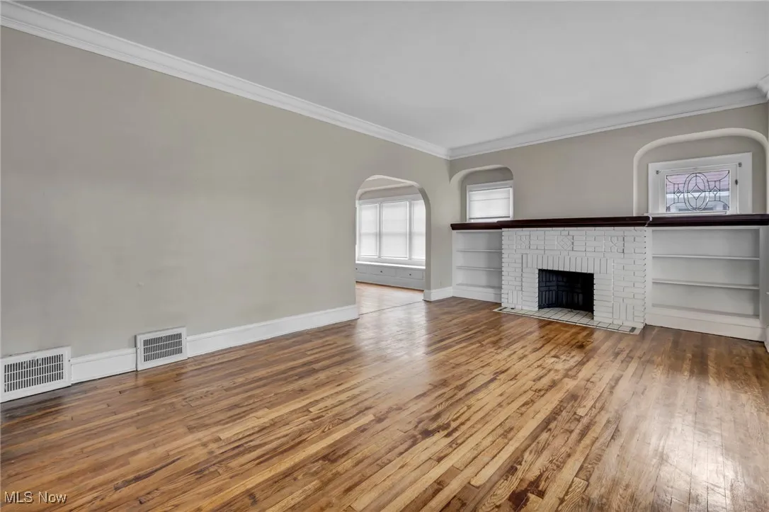Unfurnished living room with hardwood / wood-style floors, visible vents, and ornamental molding