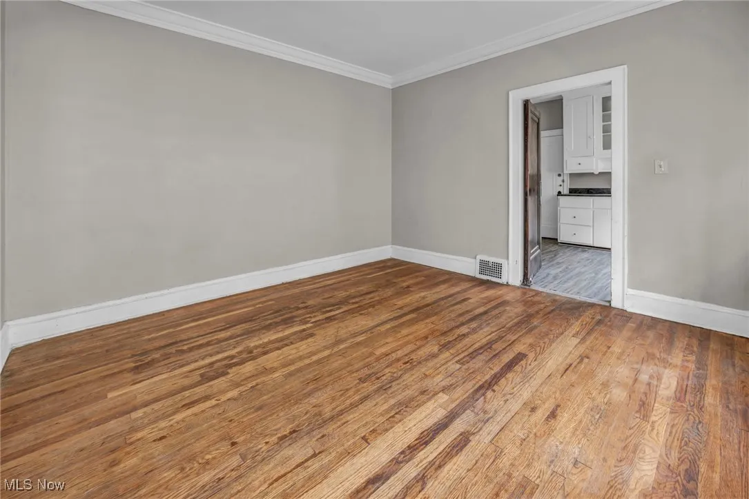 Unfurnished room featuring baseboards, wood finished floors, visible vents, and crown molding