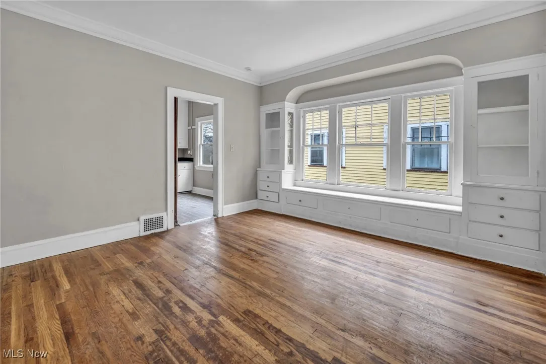 Empty room featuring wood finished floors, visible vents, baseboards, and ornamental molding
