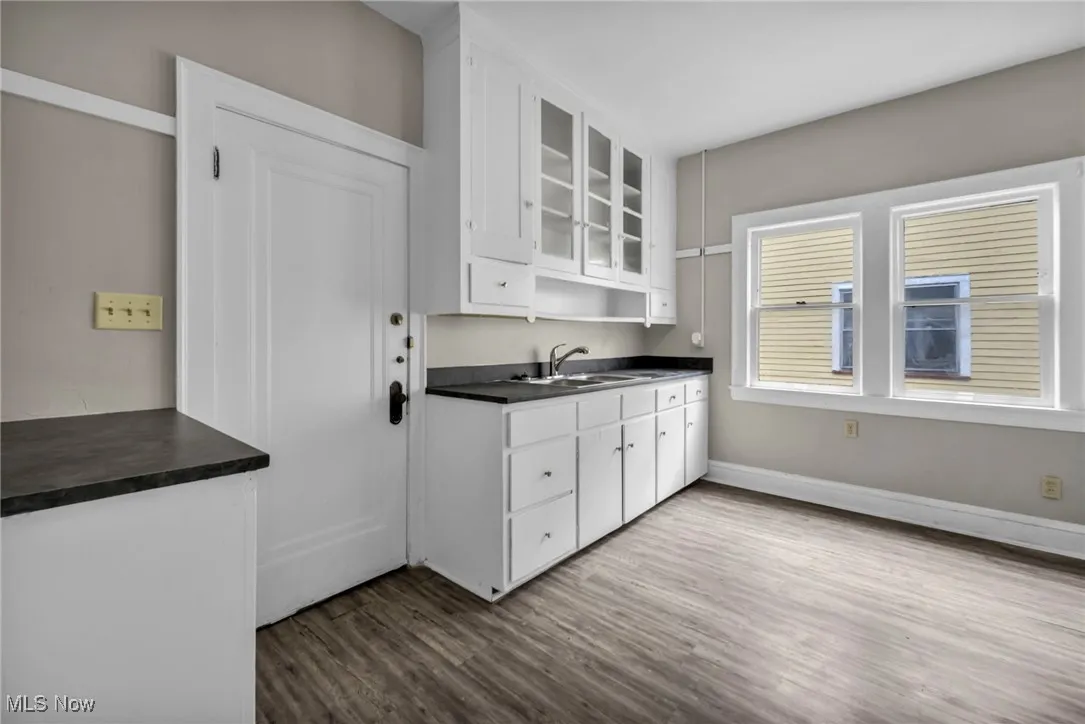 Kitchen featuring white cabinets, dark countertops, dark wood-style flooring, and a sink
