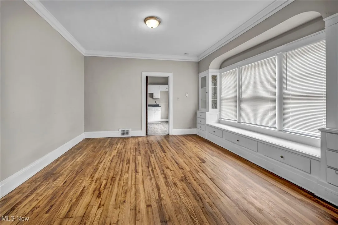 Empty room with baseboards, wood finished floors, visible vents, and ornamental molding