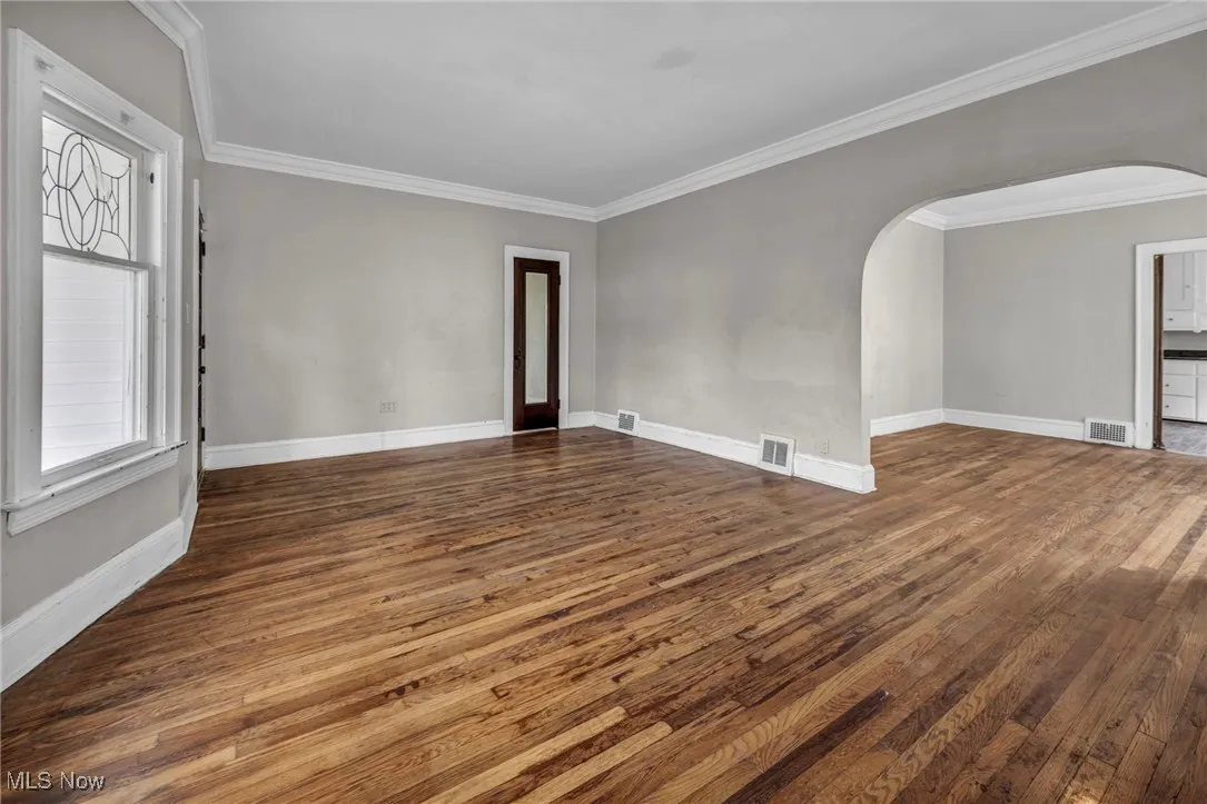 Spare room with arched walkways, visible vents, and dark wood-style flooring