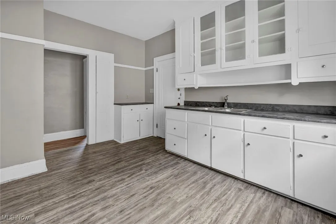 Kitchen featuring white cabinets, dark countertops, wood finished floors, and a sink