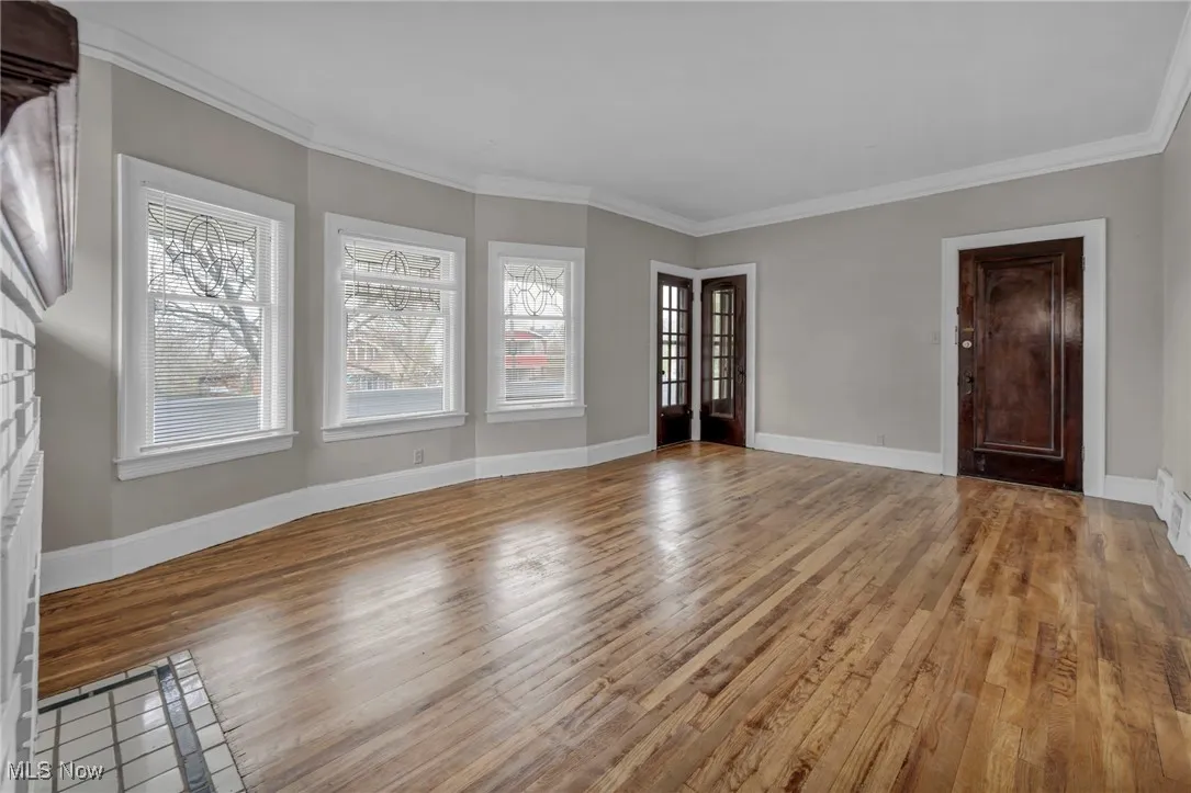 Unfurnished living room featuring baseboards, ornamental molding, and wood finished floors