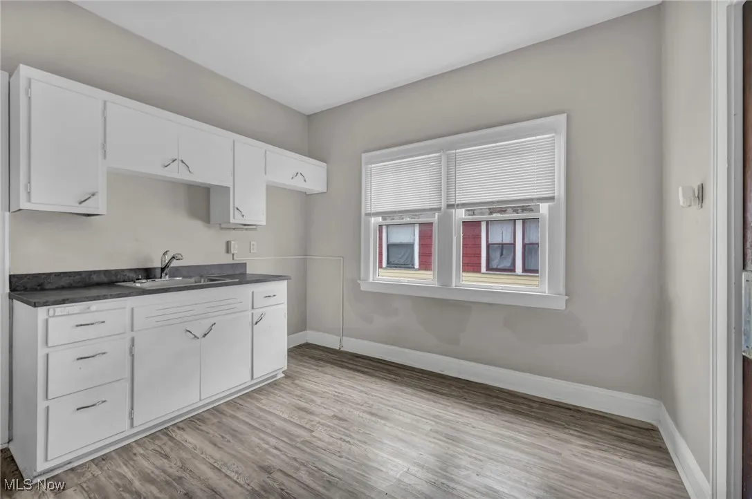 Kitchen featuring light wood finished floors, dark countertops, baseboards, and a sink