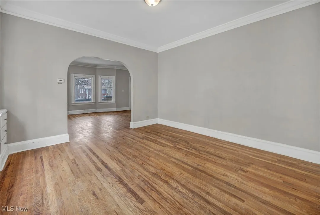 Empty room featuring wood finished floors, baseboards, arched walkways, and ornamental molding
