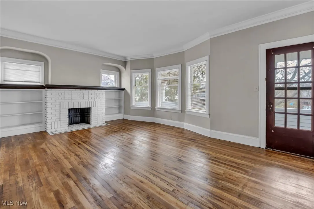 Unfurnished living room with arched walkways, baseboards, wood finished floors, crown molding, and a fireplace