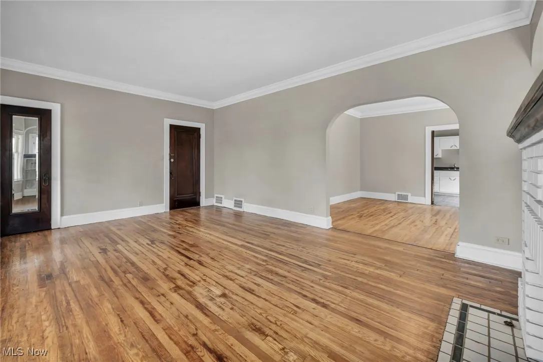 Unfurnished living room featuring wood-type flooring, arched walkways, visible vents, and crown molding