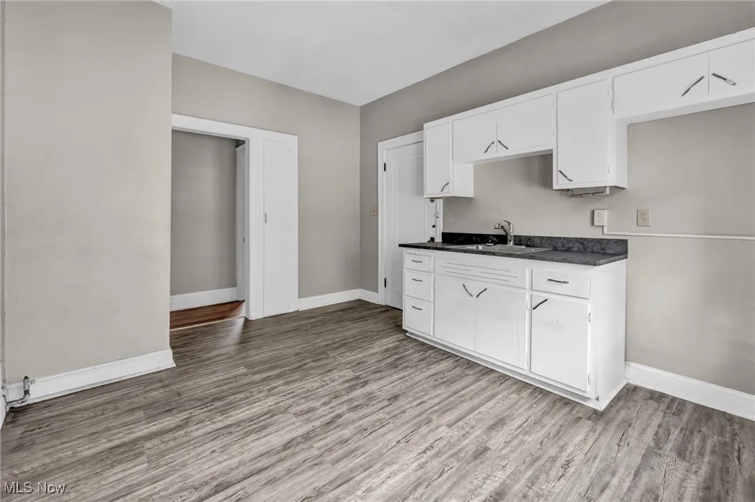 Kitchen featuring baseboards, dark countertops, wood finished floors, and a sink