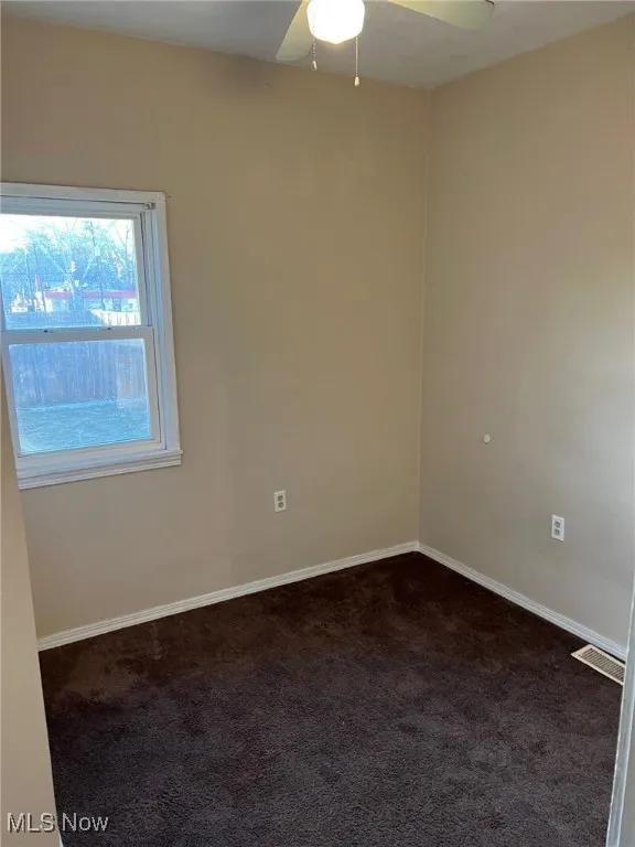 Empty room with baseboards, visible vents, ceiling fan, and carpet