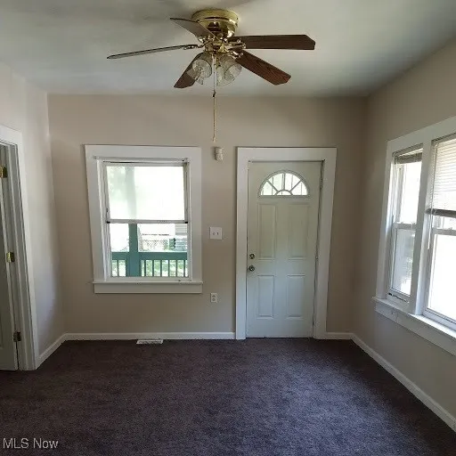Entryway with ceiling fan, baseboards, and dark colored carpet