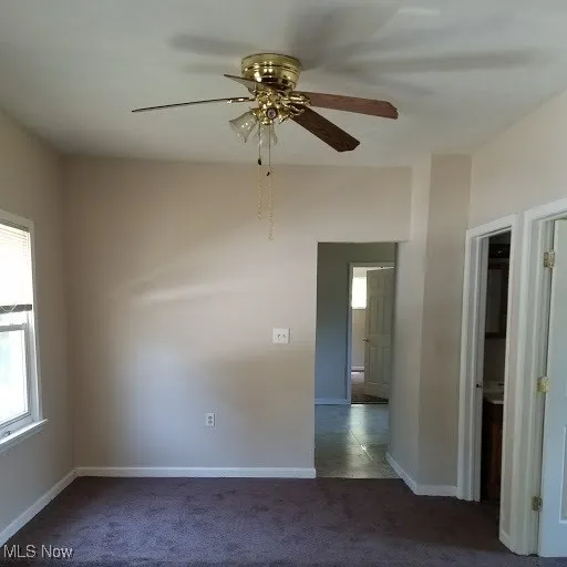 Empty room with ceiling fan, dark colored carpet, and baseboards