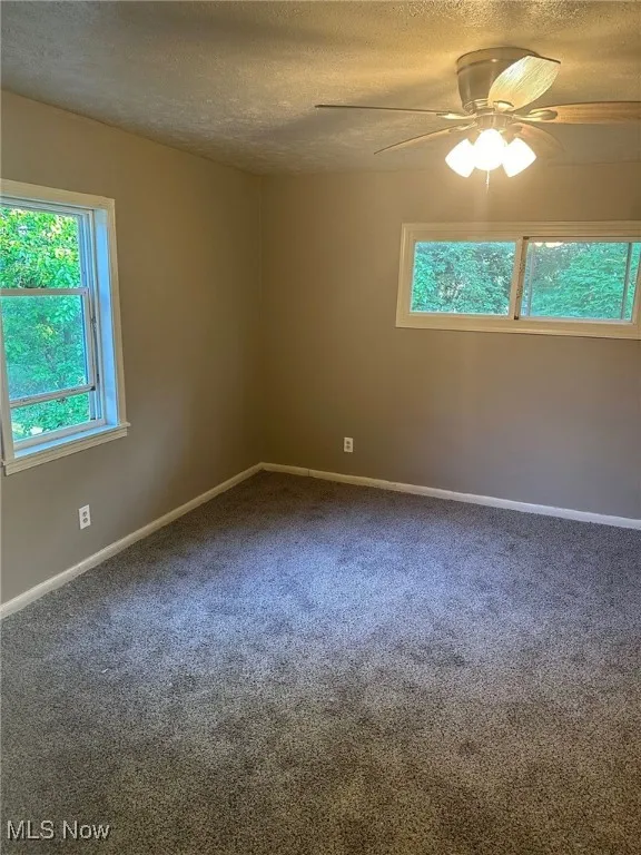 Carpeted spare room with a textured ceiling, a ceiling fan, and baseboards